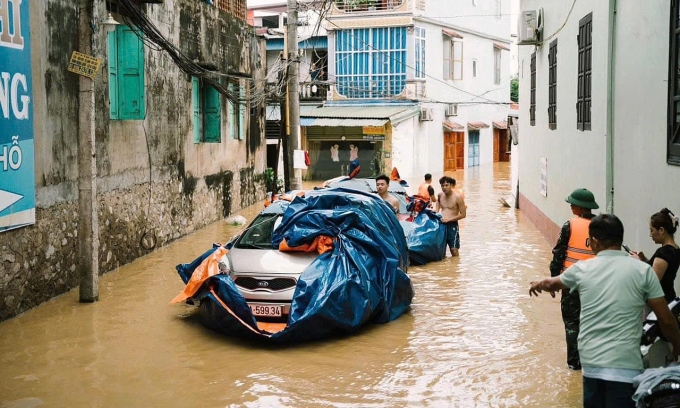 Người dân cùng lực lượng chức năng hỗ trợ kéo 2 chiếc xe của gia đình cô ra chỗ an toàn trong dòng nước lụt. Ảnh: Thiên Lý